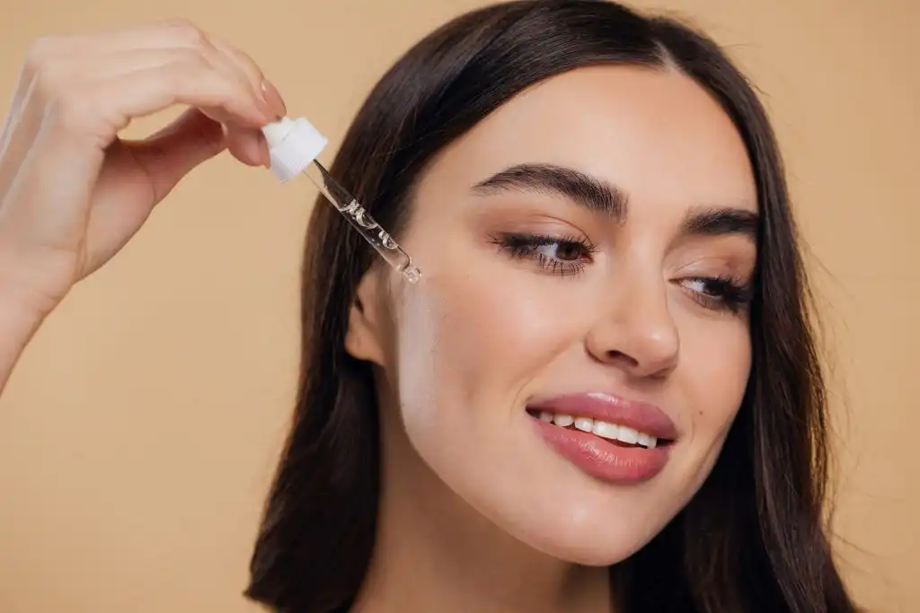 Woman Dropping Serum on Face on Beige Background